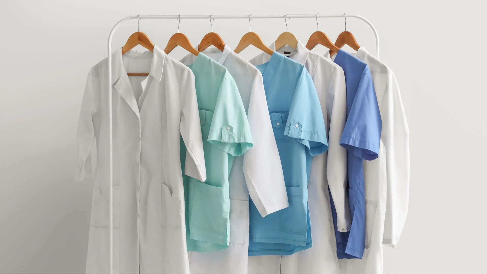 Jalecos hospitalares por função e cor – UniAlpha Uniformes Sorocaba Jalecos hospitalares nas cores branco, verde e azul pendurados em arara – padrão de cores por função conforme ANVISA